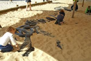 Uitgraafplaats in een grote zandbak waar kinderen een levensgroot dinoskelet blootleggen als ware archeologen en paleontologen .